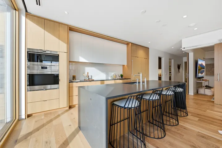 Gourmet kitchen featuring a large central island with seating, wood-finish flooring, integrated stainless steel appliances, light wood-finish cabinetry, and recessed lighting