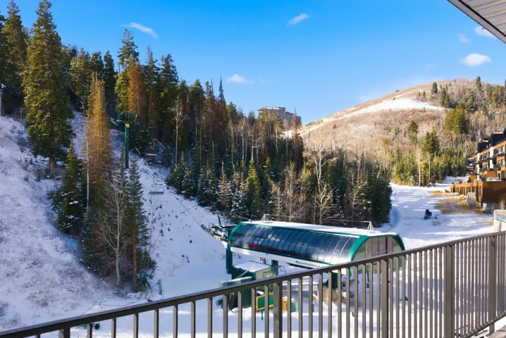 Balcony with metal railing providing alpine slope access with a ski lift, surrounded by snow-covered evergreen trees and distant mountain ranges