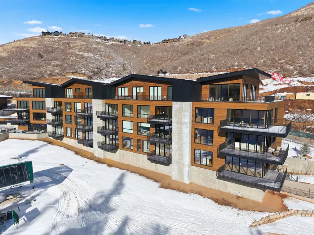 Modern multi-story building featuring wood-panel siding, concrete accents, multiple balconies with glass railings, and expansive windows