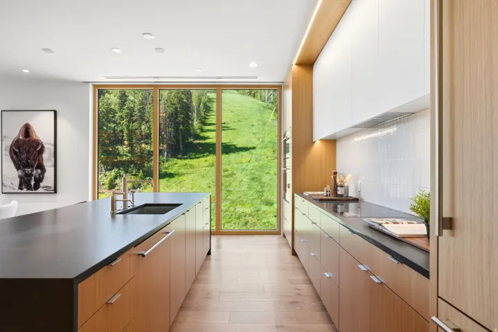 Modern kitchen featuring full-height glass paneling, wood-finish flooring, and a large center island with an undermount sink