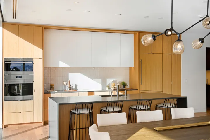 Modern kitchen featuring light wood-finish cabinetry, white upper cabinets, and a complementary tile backsplash