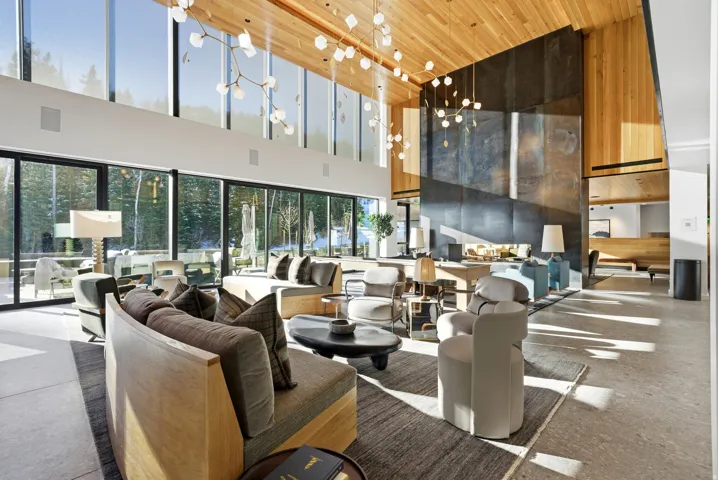 Spacious living area featuring floor-to-ceiling windows, a high vaulted wood-paneled ceiling, a large dark stone accent wall, and contemporary lighting fixtures