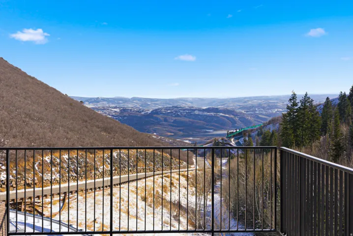 Mountain landscape featuring a distant valley, winding road, and evergreen trees