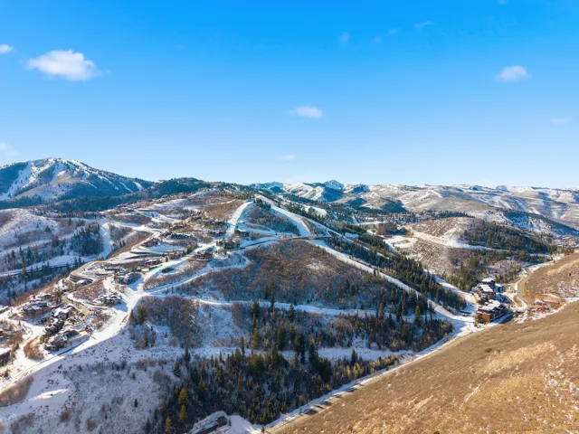 Expansive mountain landscape featuring snow-covered peaks, scattered evergreen trees, and visible ski runs