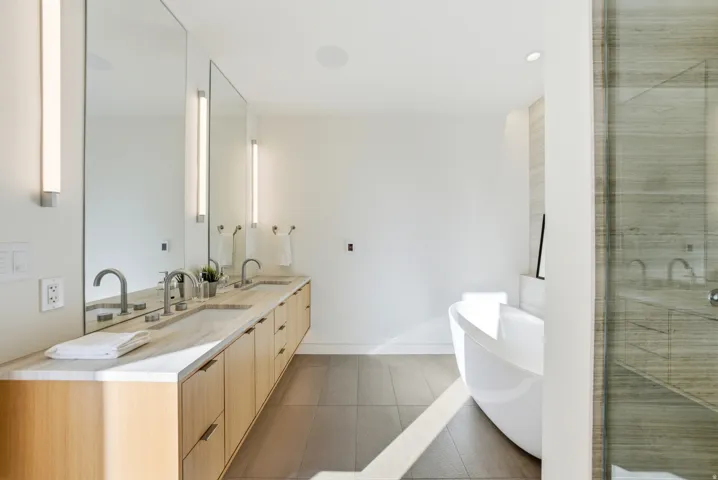Spacious bathroom featuring a dual vanity with light wood cabinetry, stone countertops, and undermount sinks