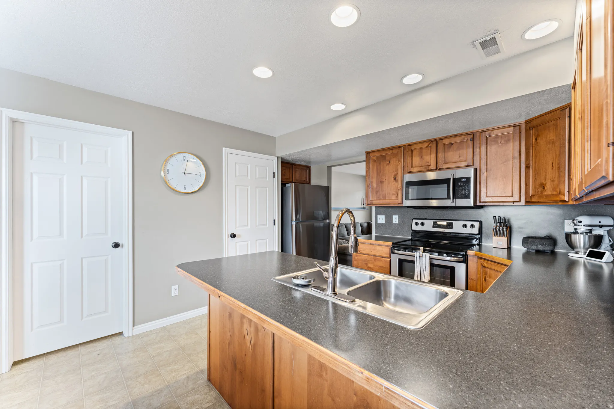 Kitchen featuring a dual basin sink with a high-arc faucet, wood-finish cabinetry, stainless steel appliances, recessed lighting, and a neutral color palette