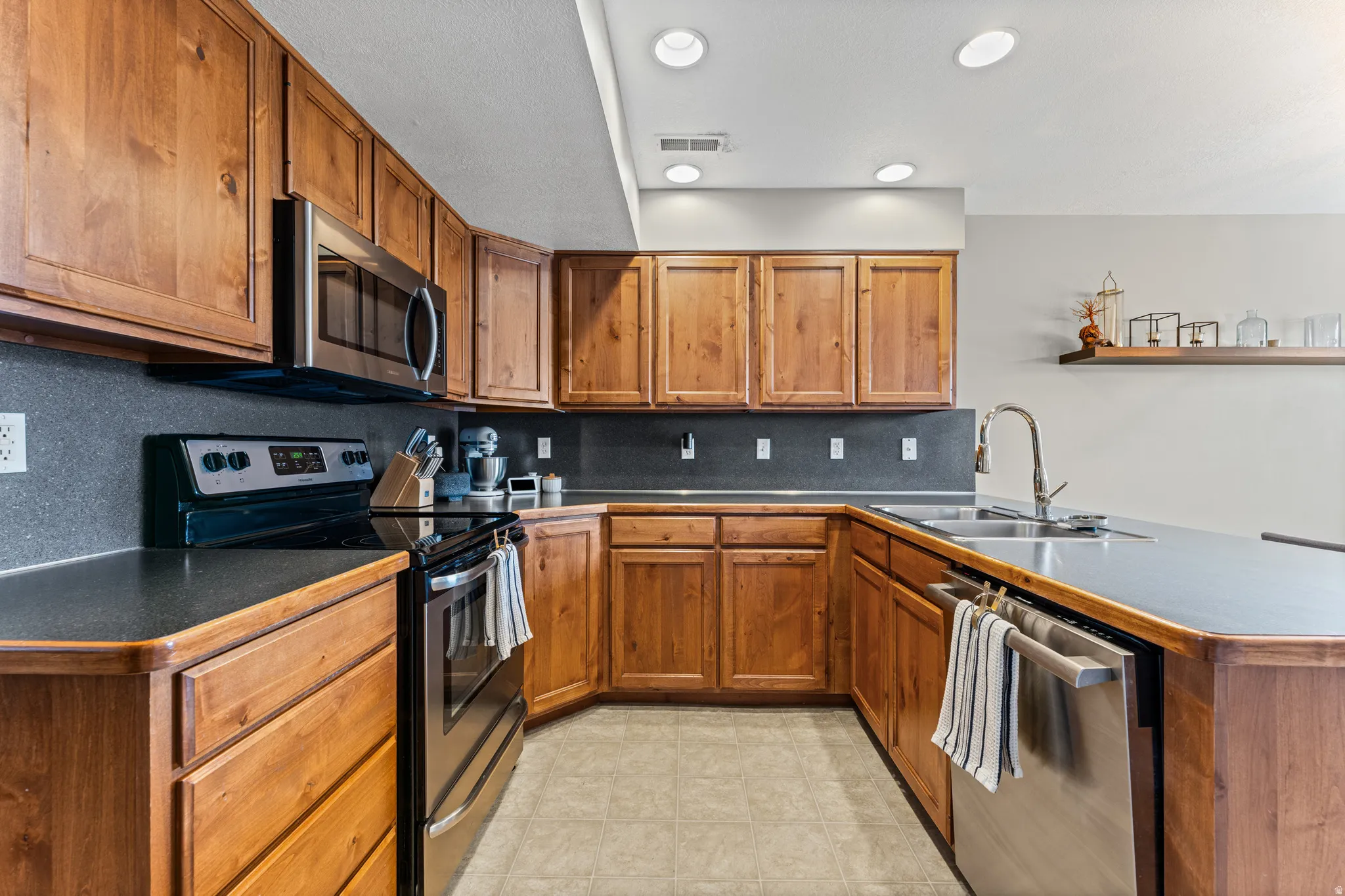U-shaped kitchen featuring wood cabinetry, stainless steel appliances, dark countertops, and recessed lighting