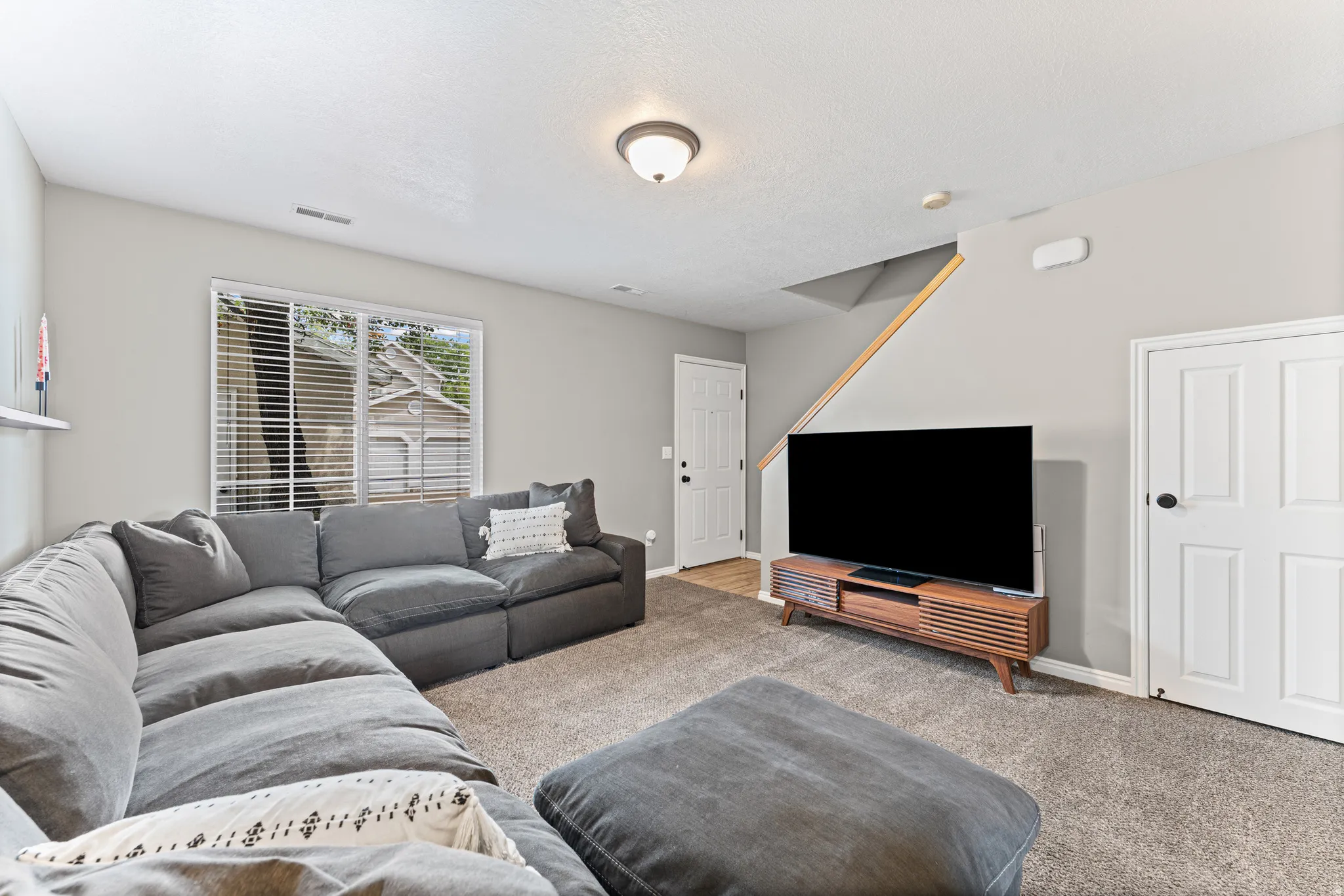 Carpeted living area featuring light gray walls, a window with blinds, and a built-in shelf