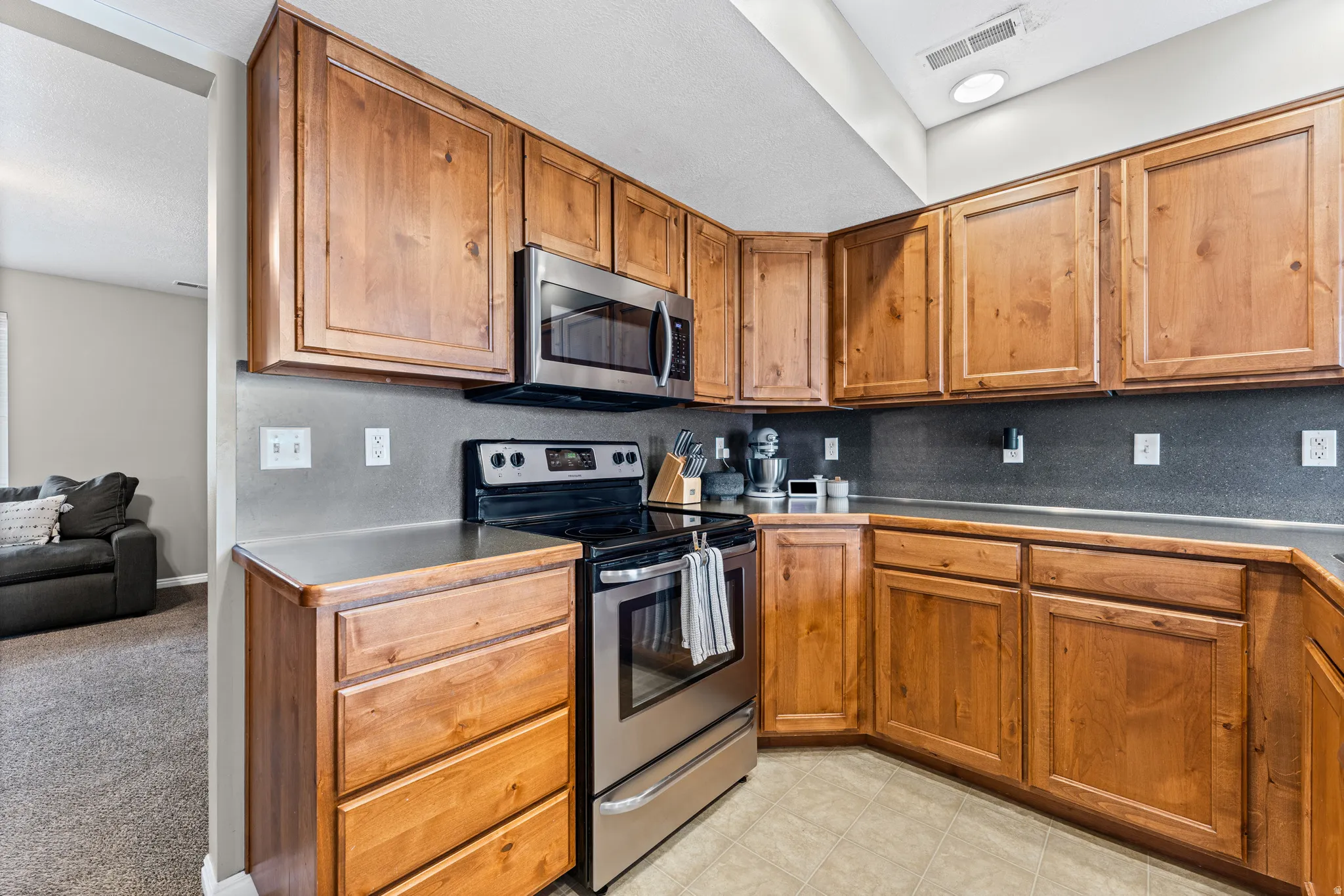 Kitchen featuring extensive natural wood cabinetry, stainless steel appliances, dark countertops, and a gray backsplash