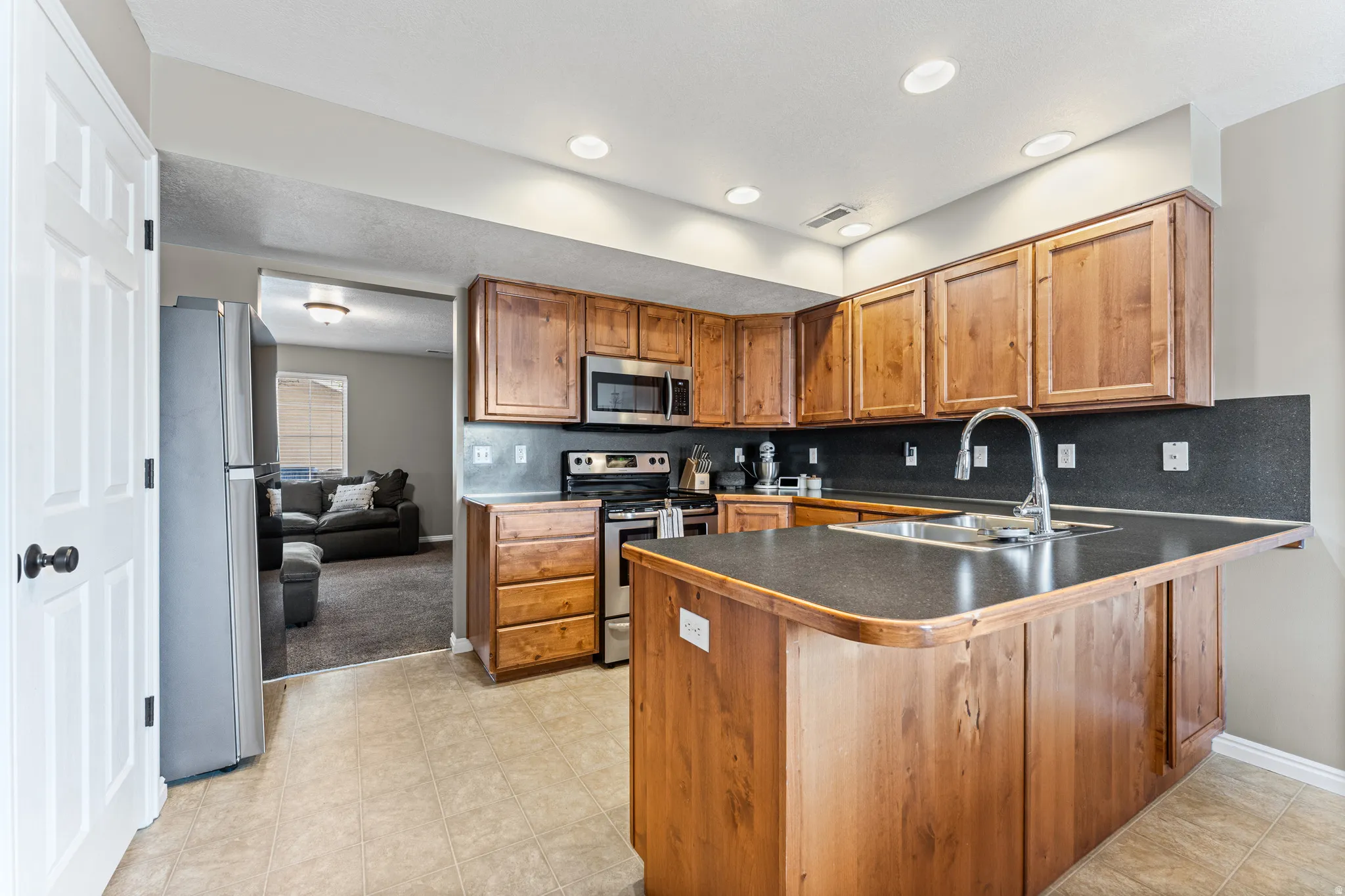 Kitchen featuring wood cabinetry, stainless steel appliances, a built-in island with a sink, recessed lighting, and tile flooring