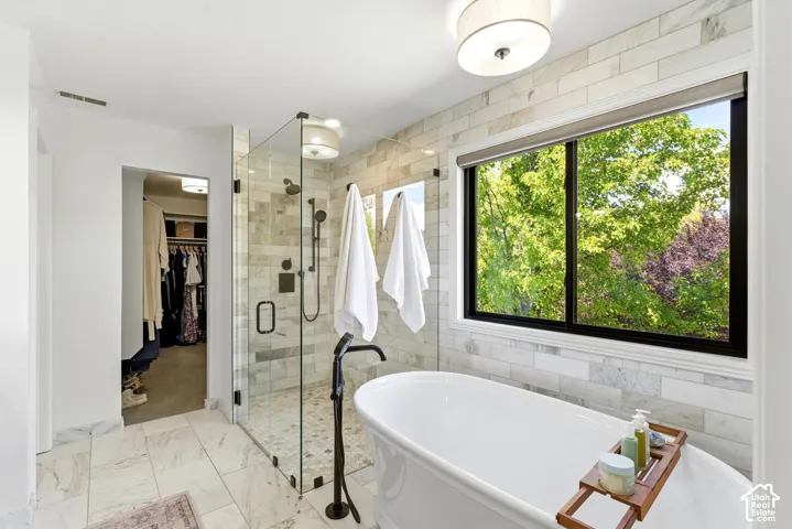 Spacious bathroom featuring a freestanding soaking tub, a glass-enclosed shower with a rainfall showerhead, and extensive tile work