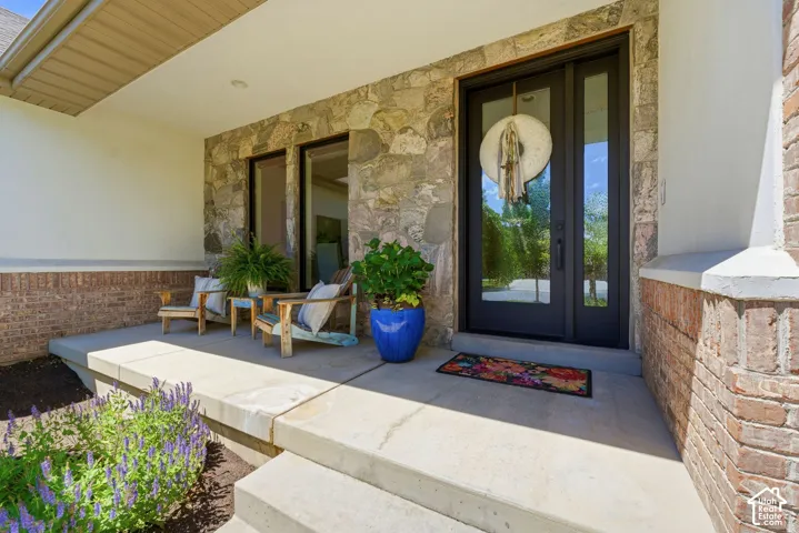 Covered front porch featuring stone and brick accents, a dark-framed entry door with sidelights, and concrete steps