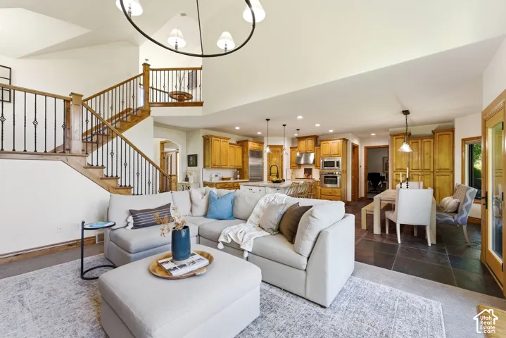 Spacious living area featuring vaulted ceilings, a grand staircase with wrought iron balusters, a large kitchen with wood cabinetry and stainless steel appliances, and a dining area with slate flooring