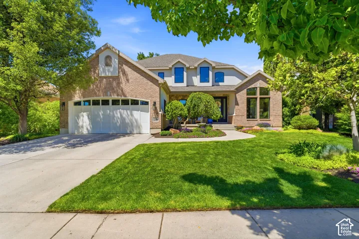 Traditional-style residence featuring a brick and stucco facade, a two-car garage, established landscaping, and a concrete driveway