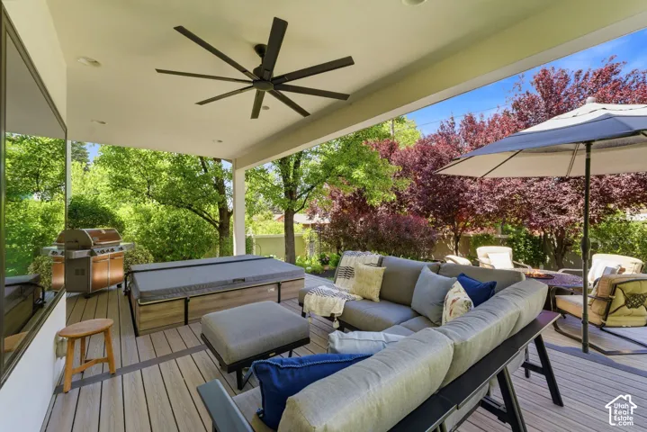 Spacious covered deck featuring a dark-bladed ceiling fan, light wood-finish decking, and a built-in outdoor spa