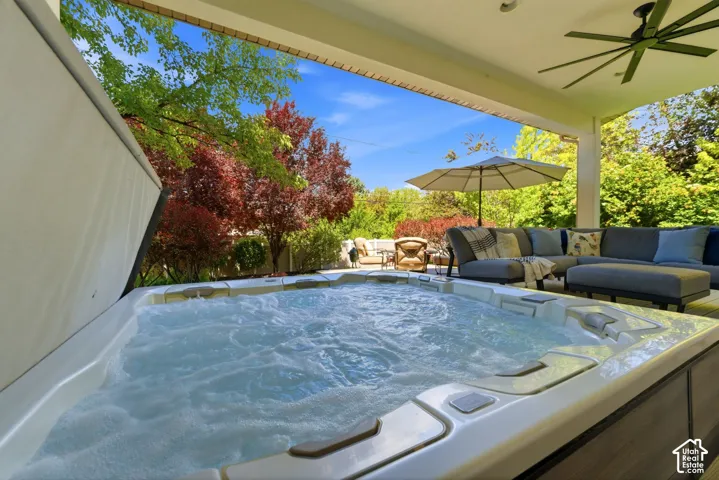 Outdoor covered patio featuring a built-in spa with bubbling water, a large ceiling fan, and surrounding mature trees