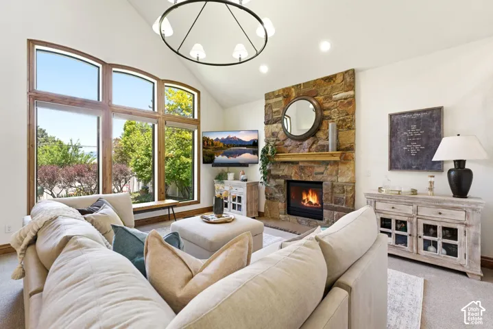 Vaulted ceiling living area featuring a stone-clad fireplace with a wood mantel, large arched windows with wood trim, recessed lighting, and a prominent chandelier