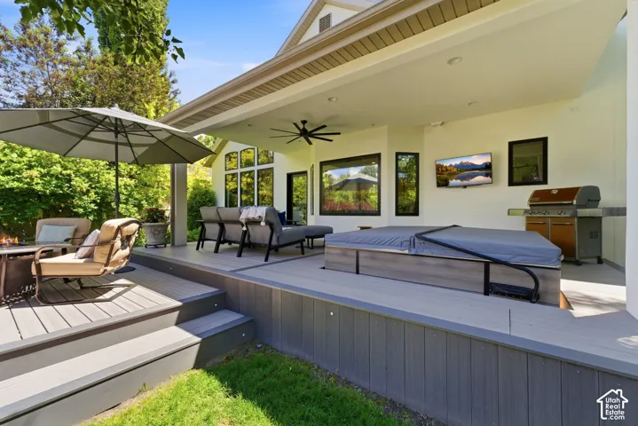 Multi-level composite deck with integrated steps, featuring an attached hot tub, covered patio with ceiling fan, and built-in outdoor kitchen space