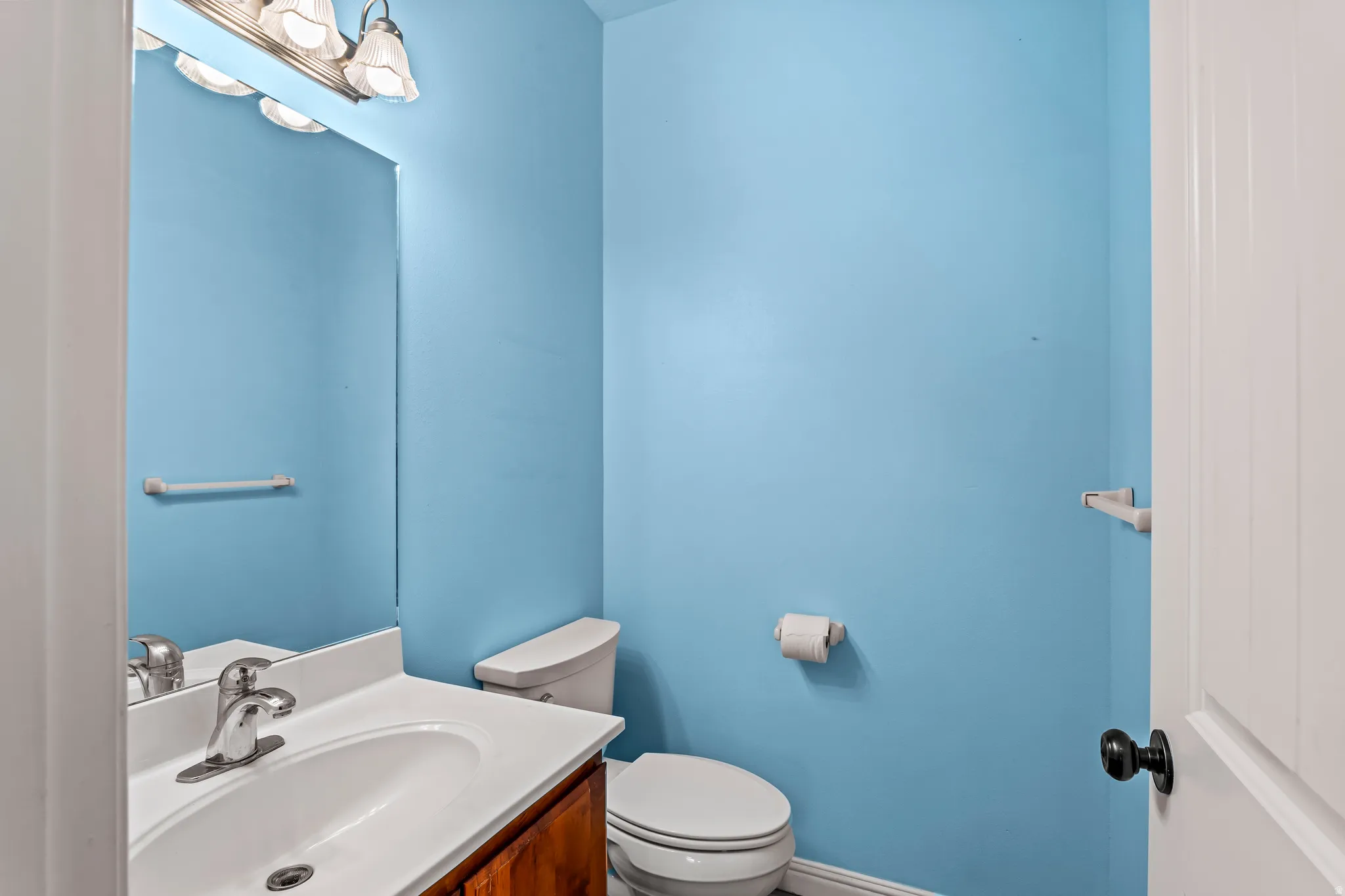 Compact bathroom featuring a wood-finish vanity with an integrated white sink, chrome faucet, and a toilet