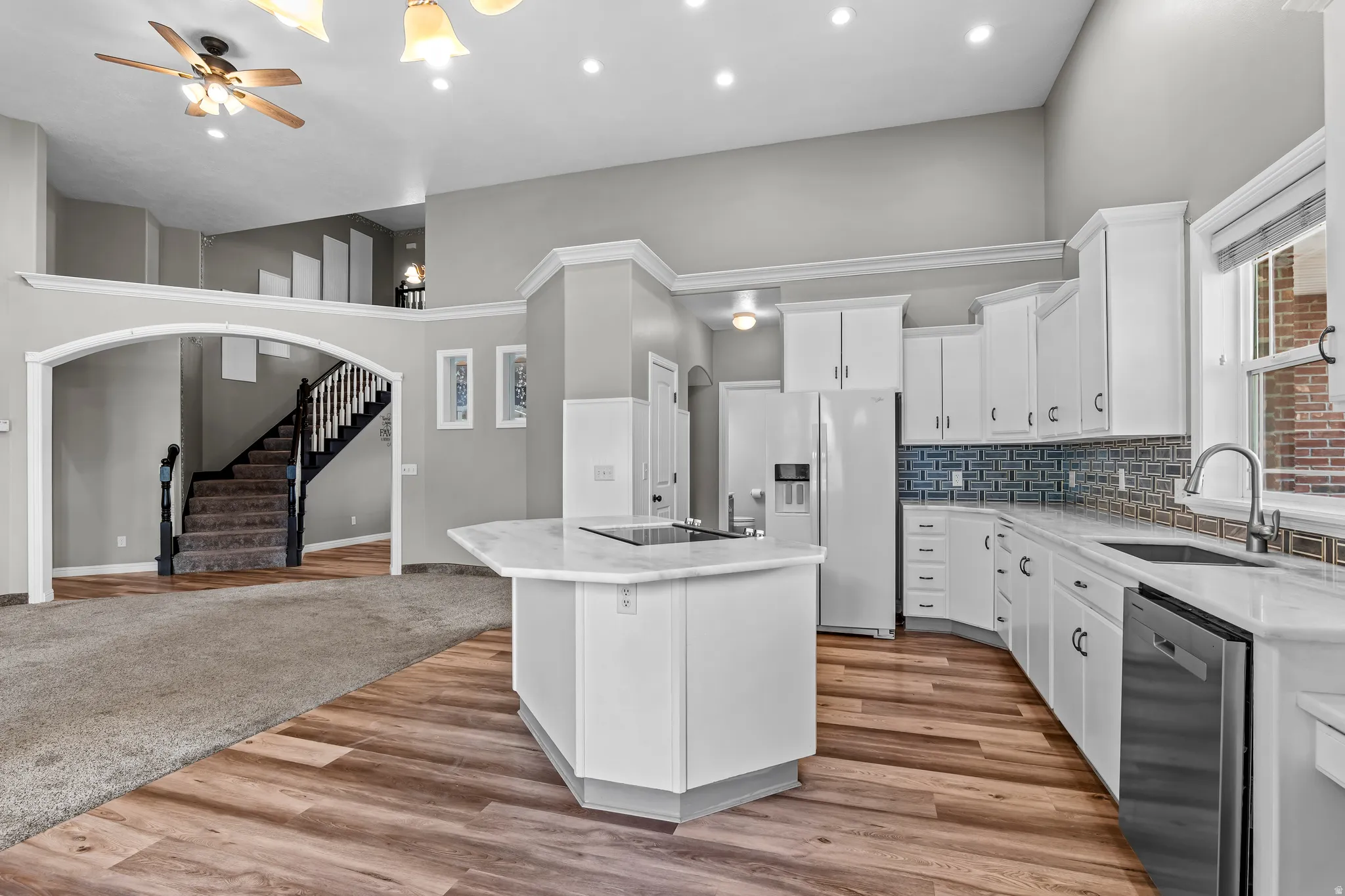 Spacious kitchen featuring white cabinetry, light-toned countertops, stainless steel appliances, a center island with a cooktop, and wood-finish flooring