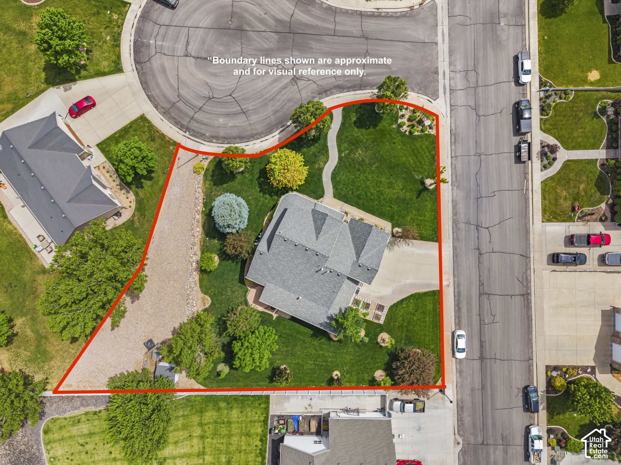 Aerial property overview featuring a large, landscaped lot with mature trees and a gravel driveway