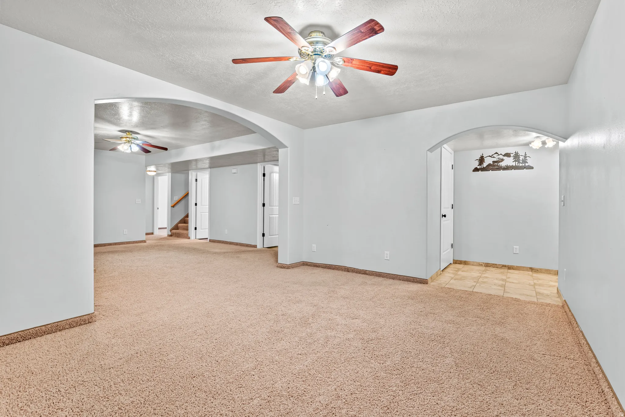 Spacious living area featuring neutral carpeting, light-toned walls, and a ceiling fan with wood-finish blades