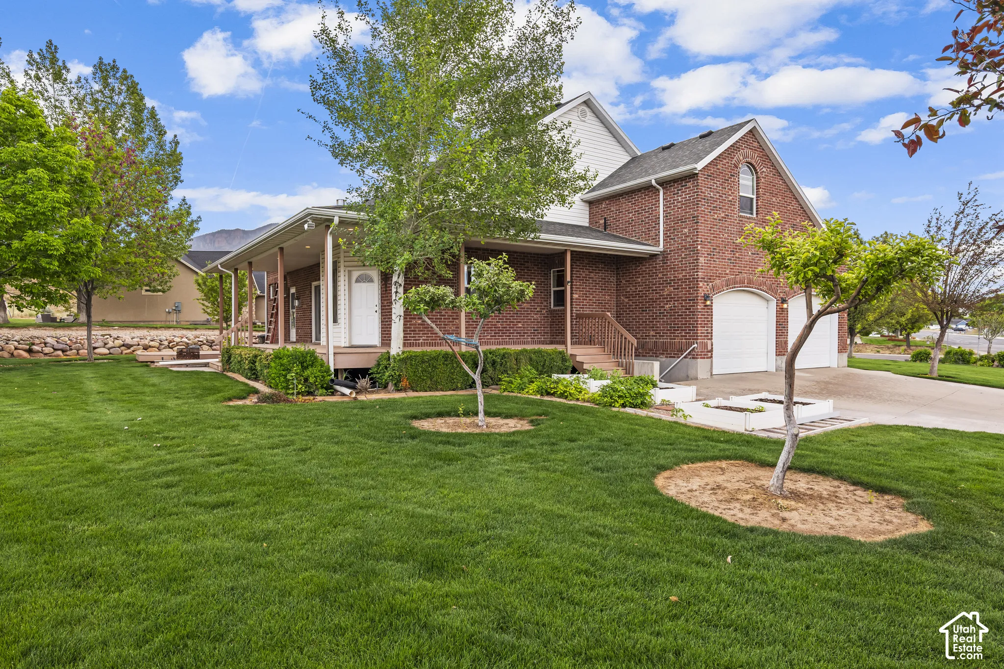 Brick and siding exterior featuring a covered porch with white columns, a two-car garage with arched entrances, mature trees, and a manicured lawn