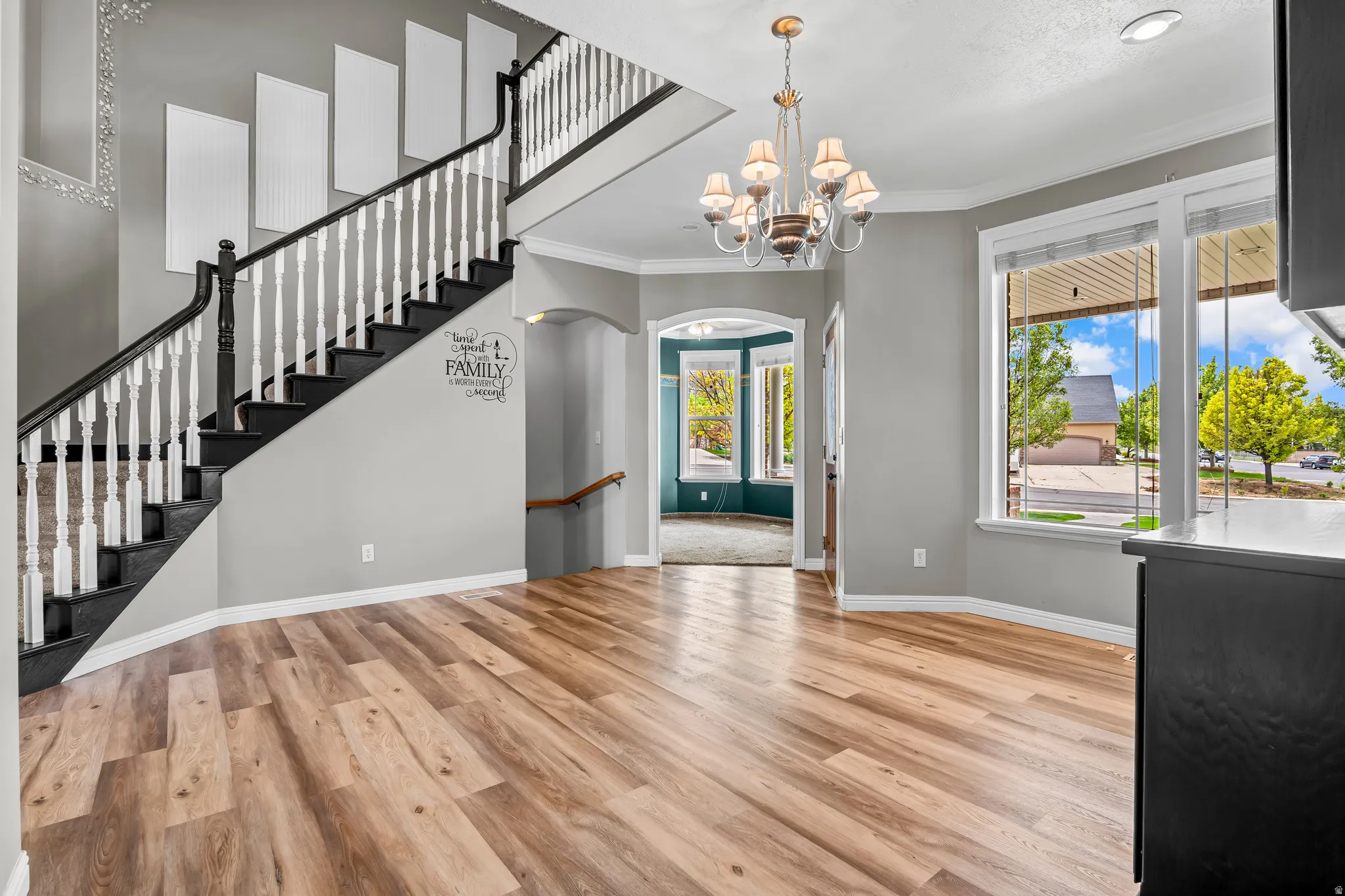 Expansive entry area featuring wood-finish flooring, a grand staircase with dark treads and white balusters, and a chandelier with glass shades