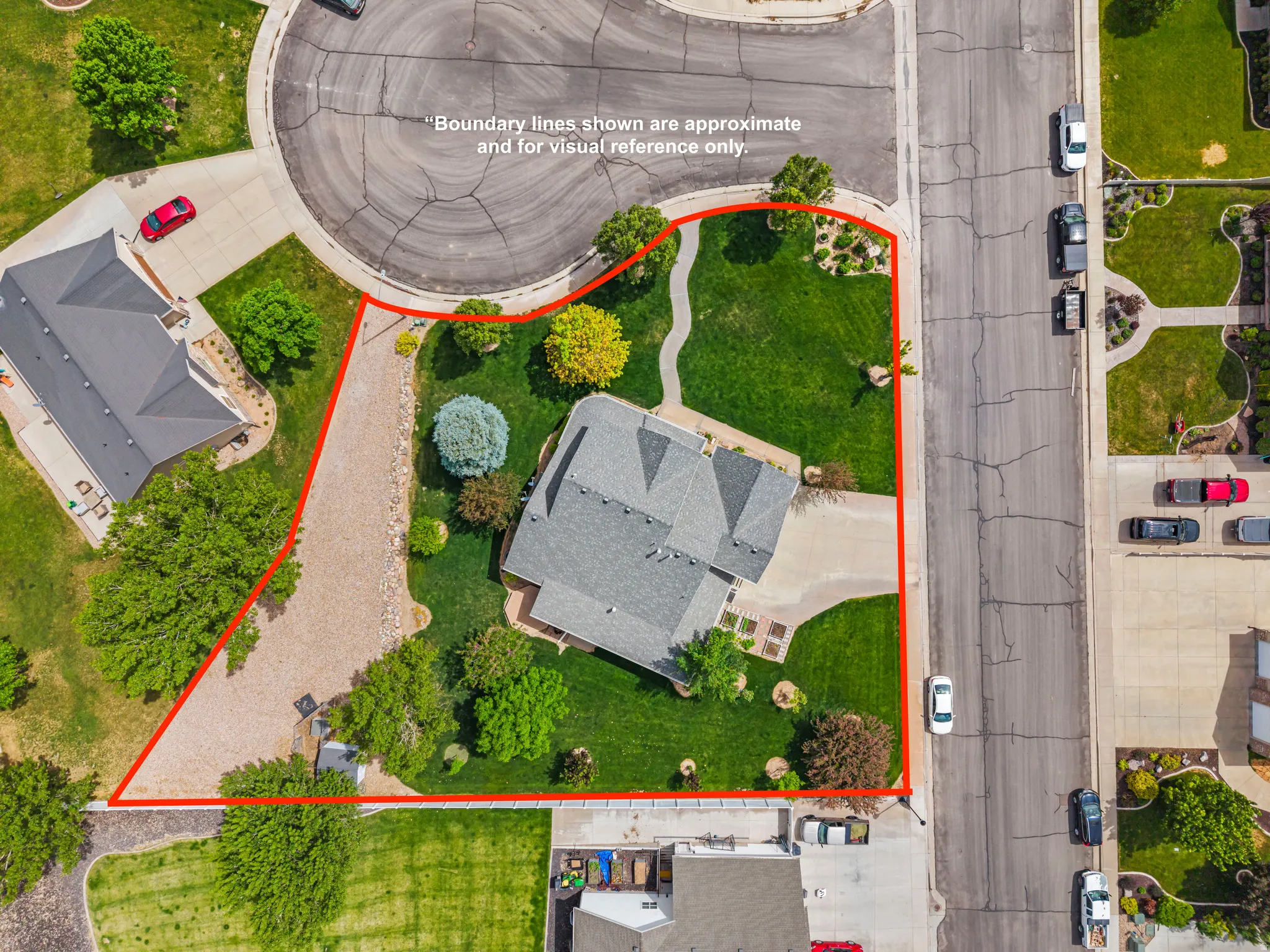 Aerial property overview featuring a large, landscaped lot with mature trees and a gravel driveway