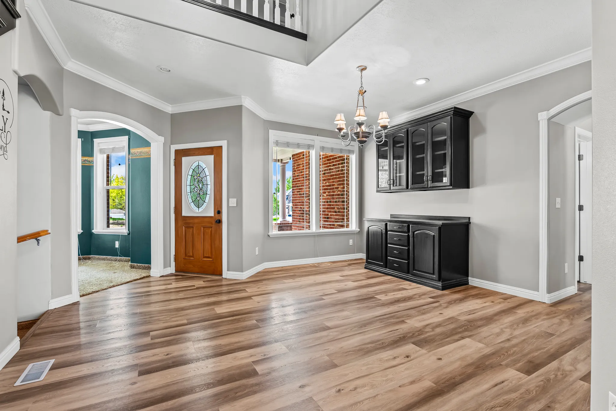 Spacious foyer entry with wood-finish flooring, a decorative oval glass front door, and a built-in black cabinetry unit