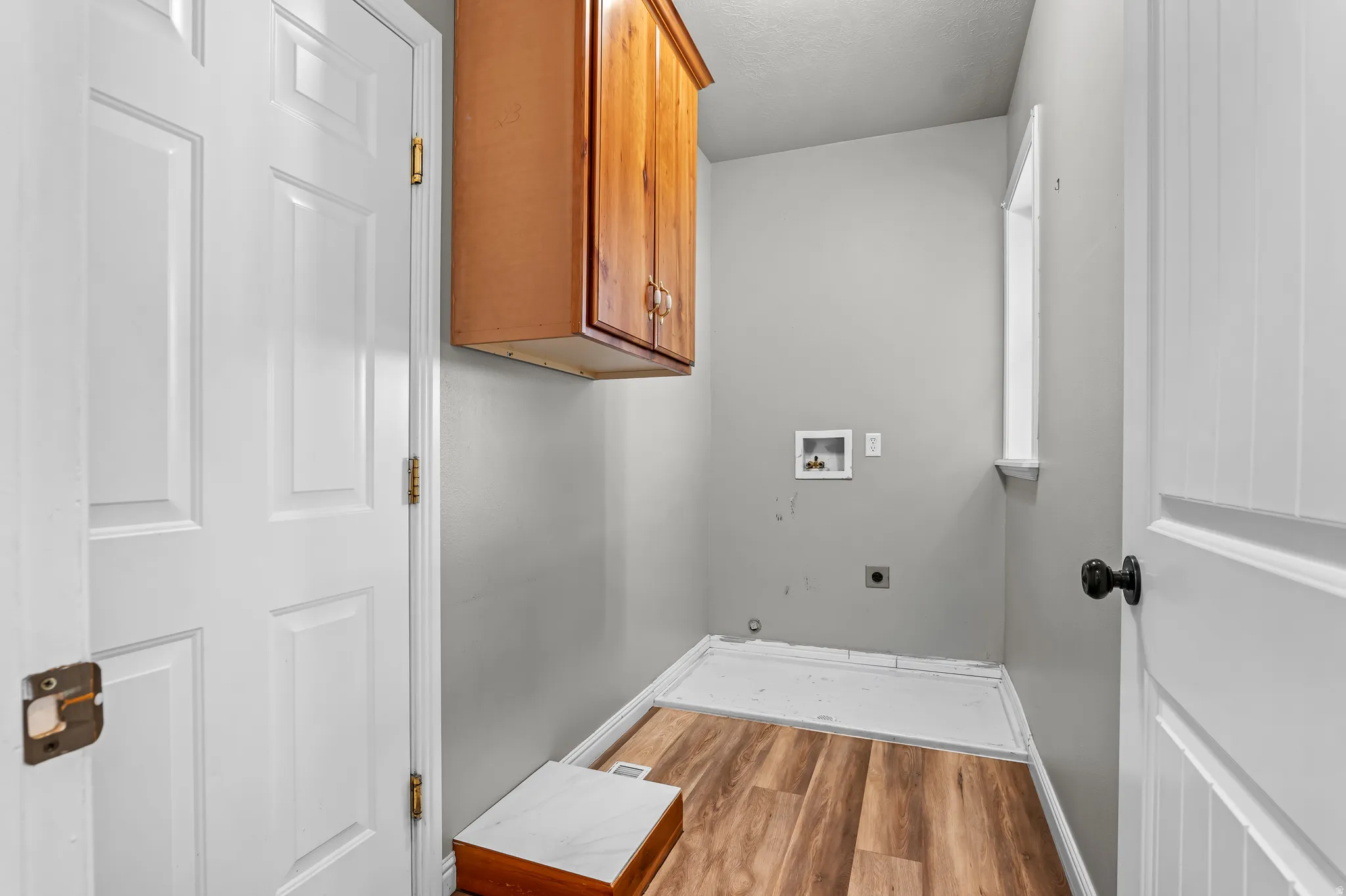 Utility space with wood-finish flooring, light gray walls, white trim, a window, and wood cabinetry