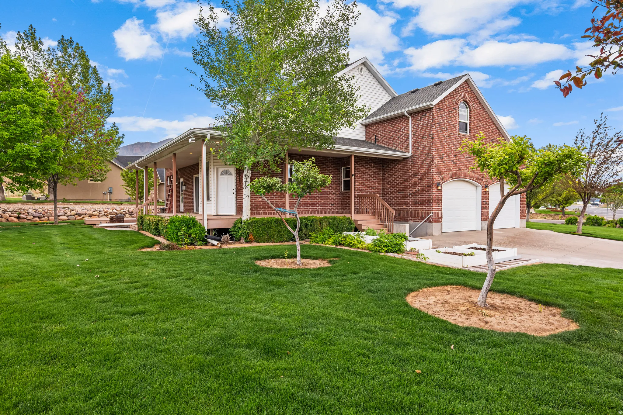 Brick and siding exterior featuring a covered porch with white columns, a two-car garage with arched entrances, mature trees, and a manicured lawn
