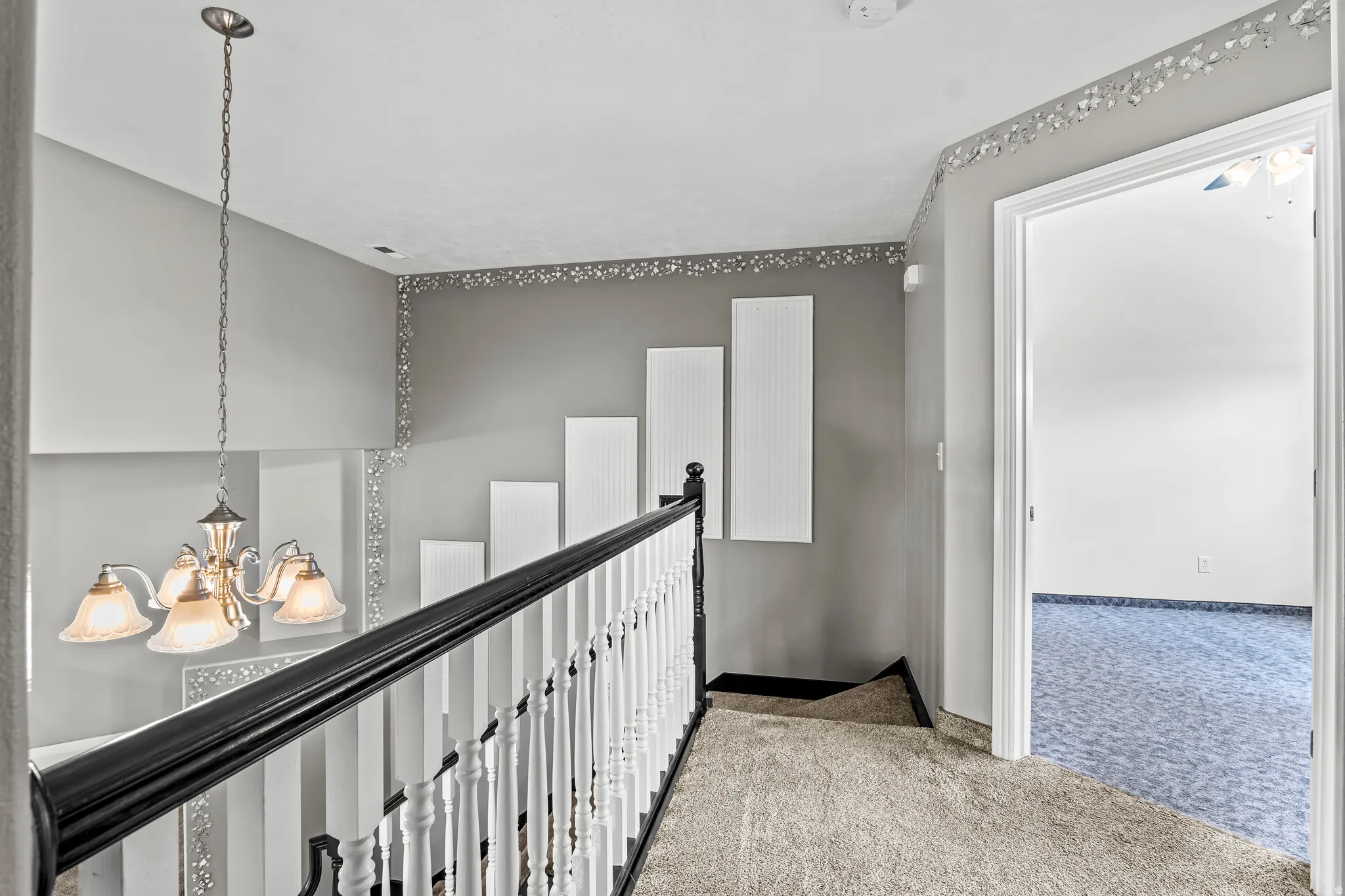 Upper-level landing featuring a chandelier, white spindle railing with a black handrail, and light gray walls