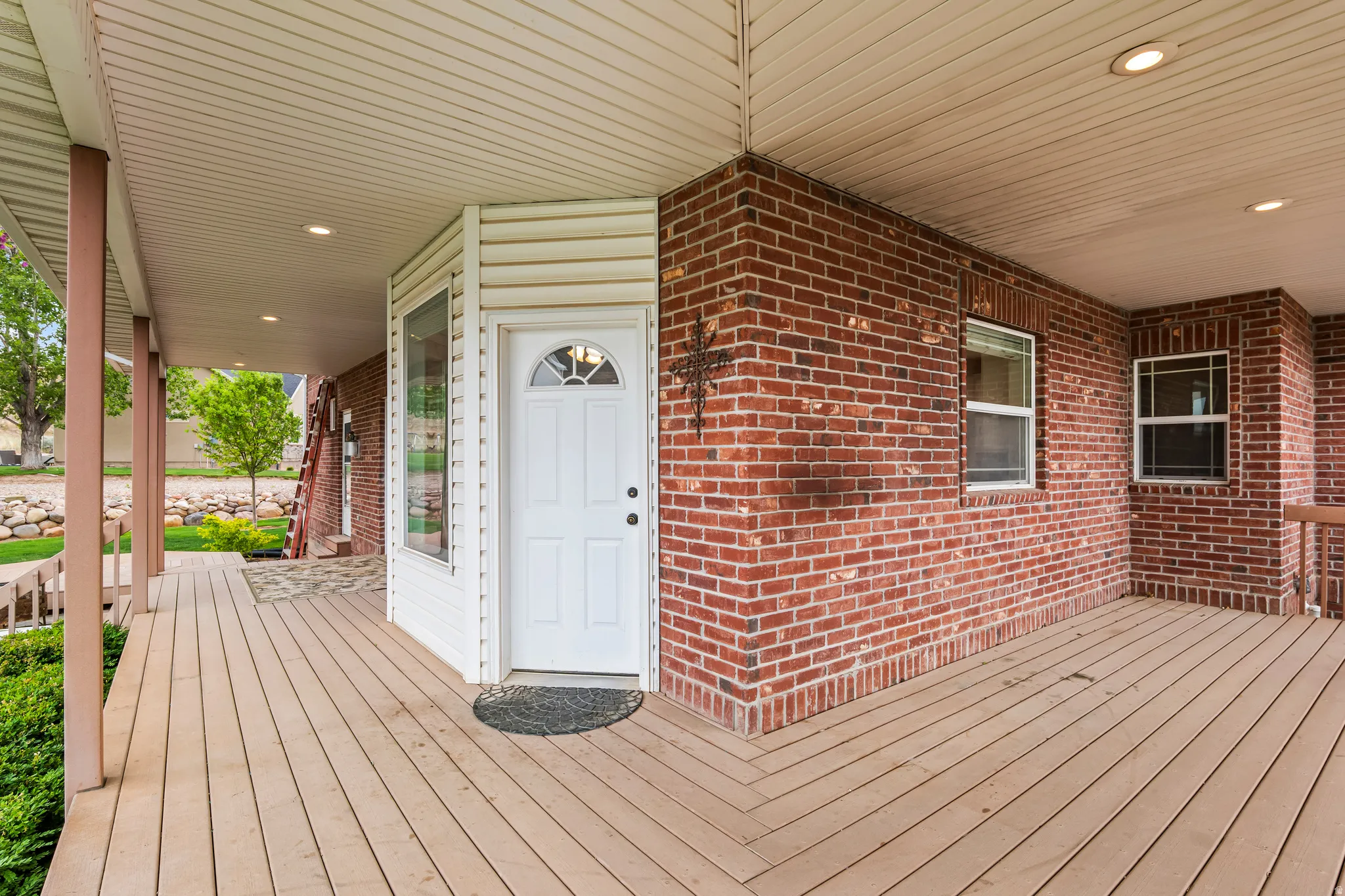 Expansive covered porch featuring wood-finish decking, recessed lighting, and brick exterior walls