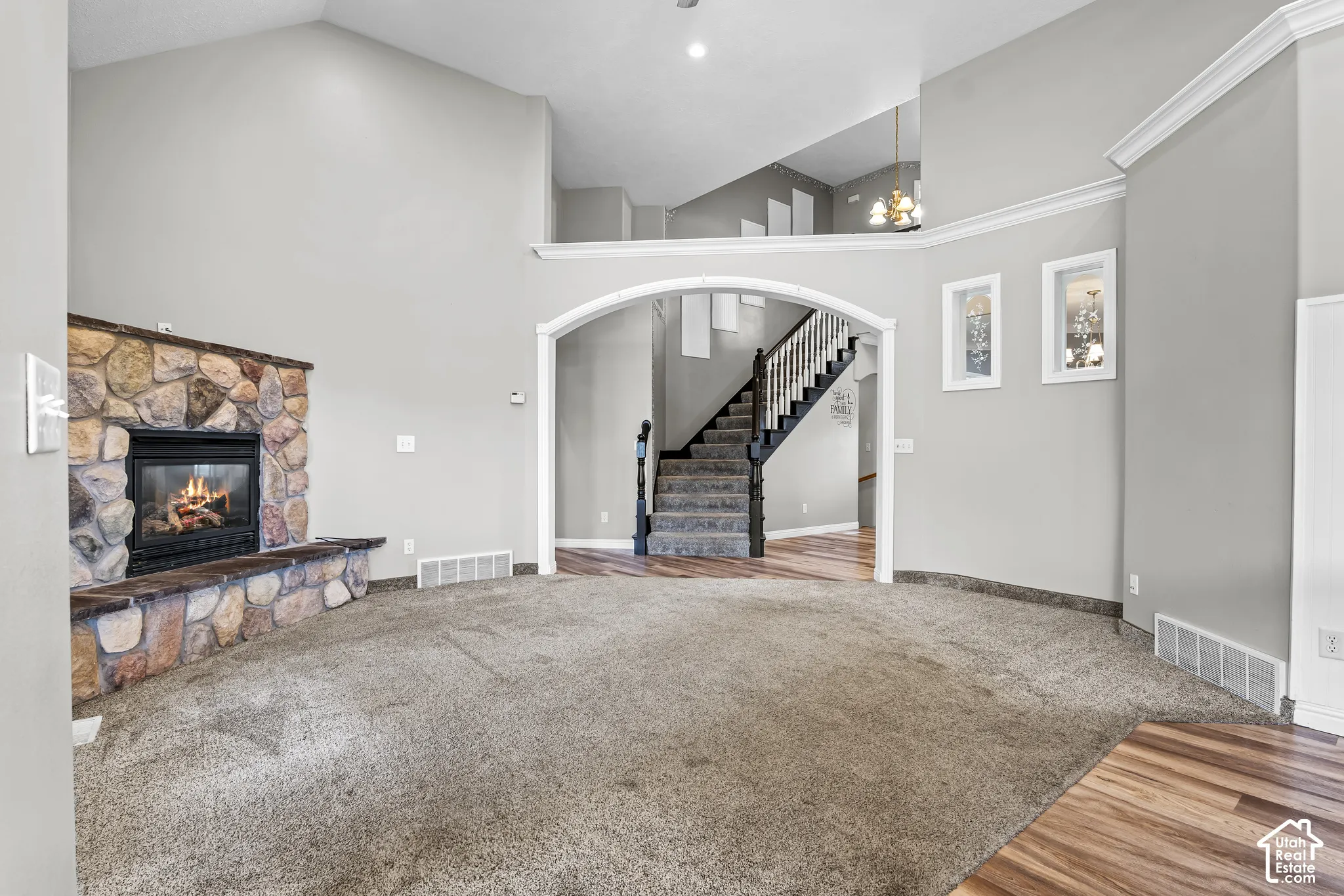 Spacious living area featuring a stone fireplace with hearth seating, vaulted ceilings, and plush carpeting