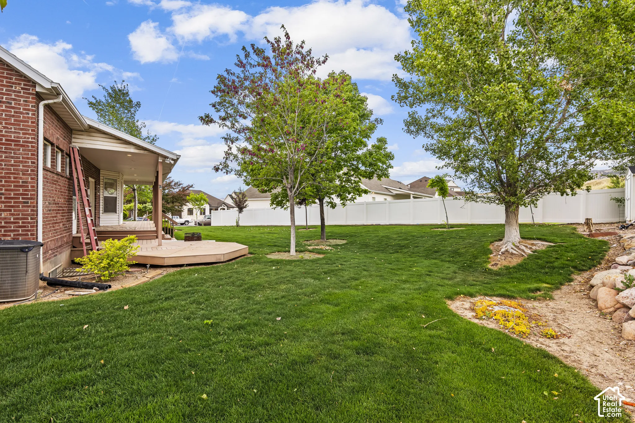 Spacious backyard featuring a covered patio, a multi-level composite deck, mature trees, and a white vinyl privacy fence