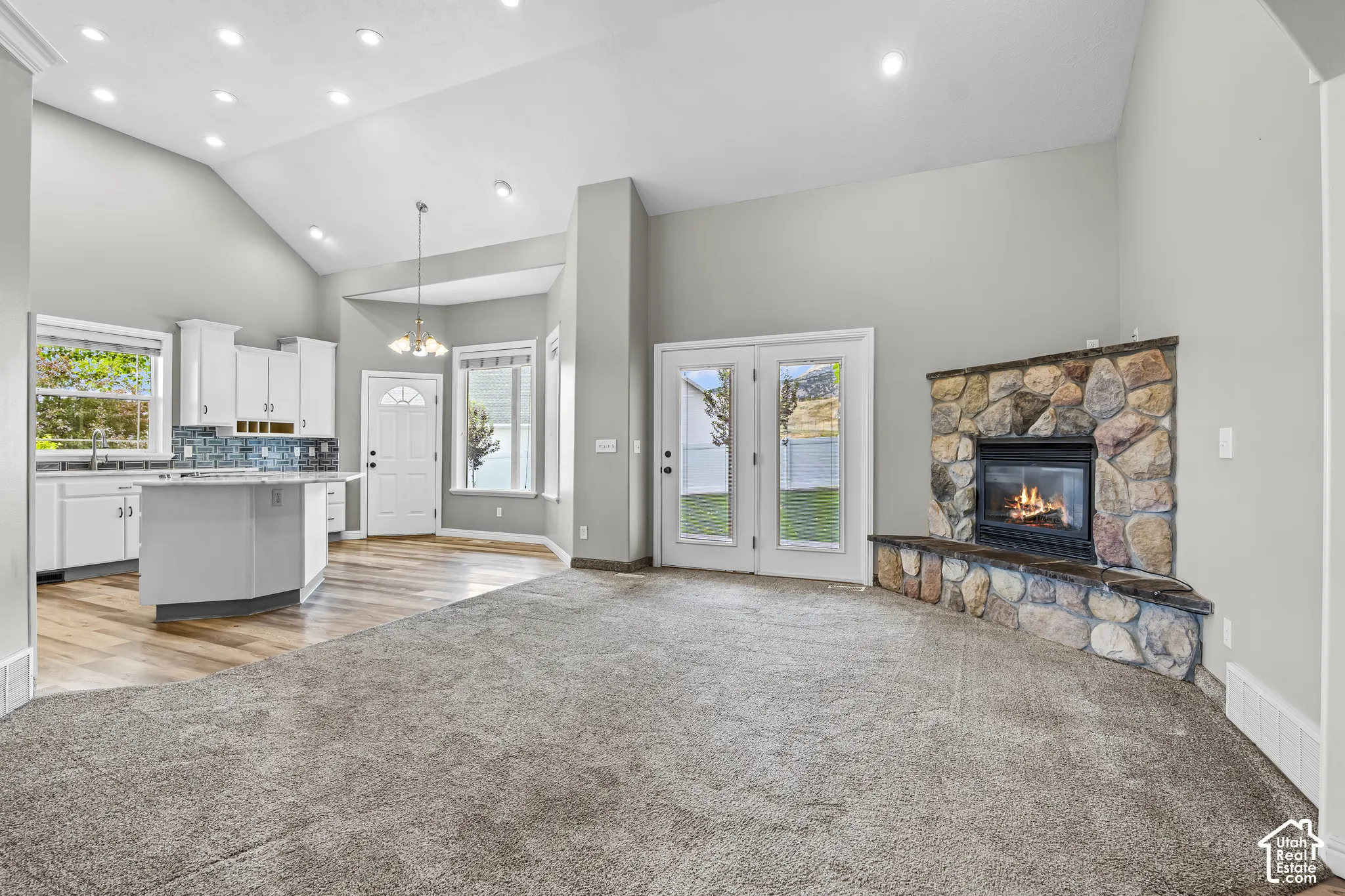 Spacious living area featuring a stone-clad fireplace and hearth, French doors, vaulted ceilings with recessed lighting, a kitchen island with seating, and wood-finish flooring