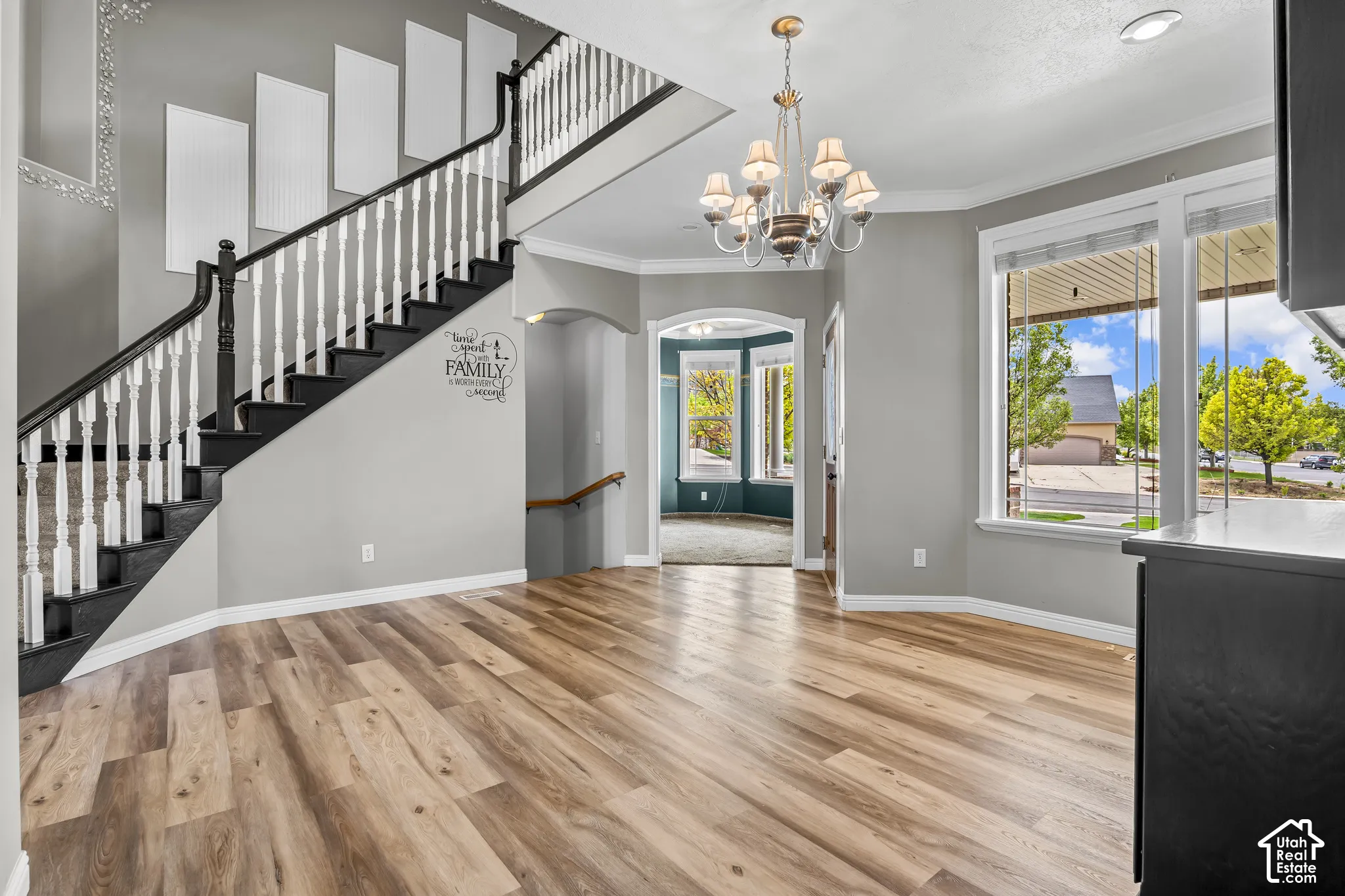 Expansive entry area featuring wood-finish flooring, a grand staircase with dark treads and white balusters, and a chandelier with glass shades