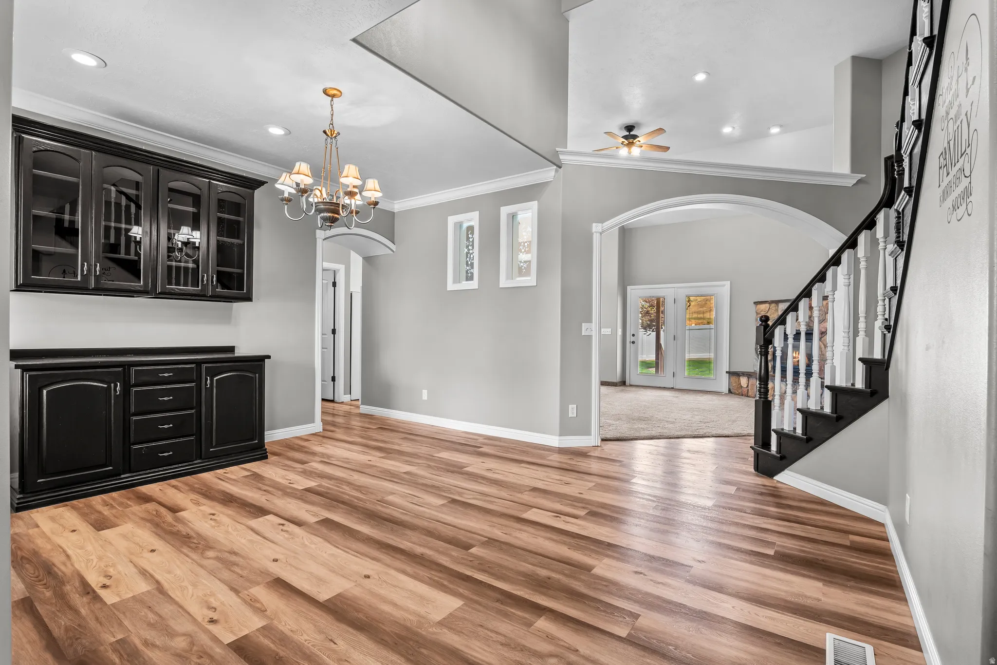 Spacious interior featuring wood-finish flooring, a built-in black cabinetry unit with glass fronts, and a decorative chandelier