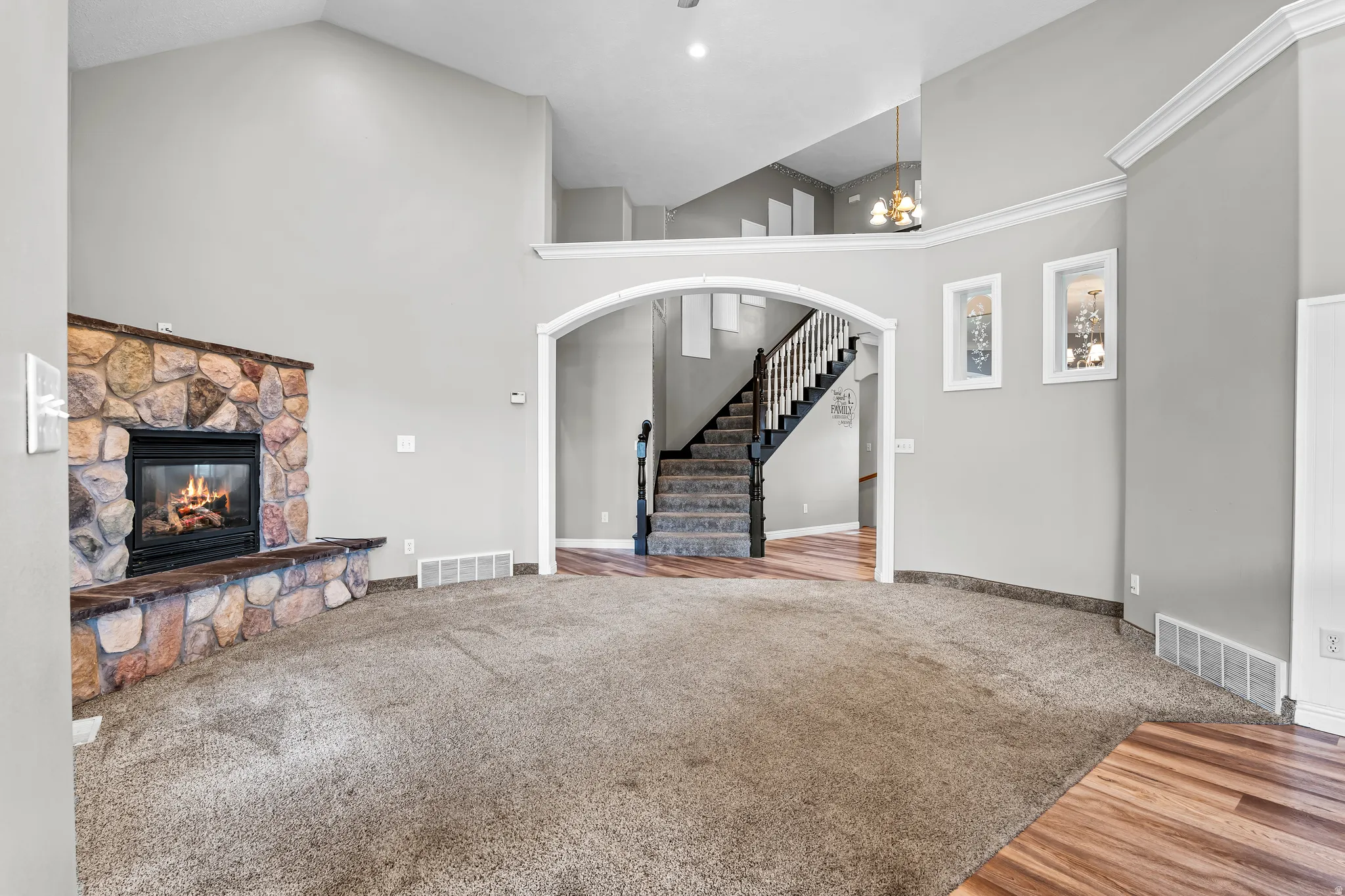 Spacious living area featuring a stone fireplace with hearth seating, vaulted ceilings, and plush carpeting