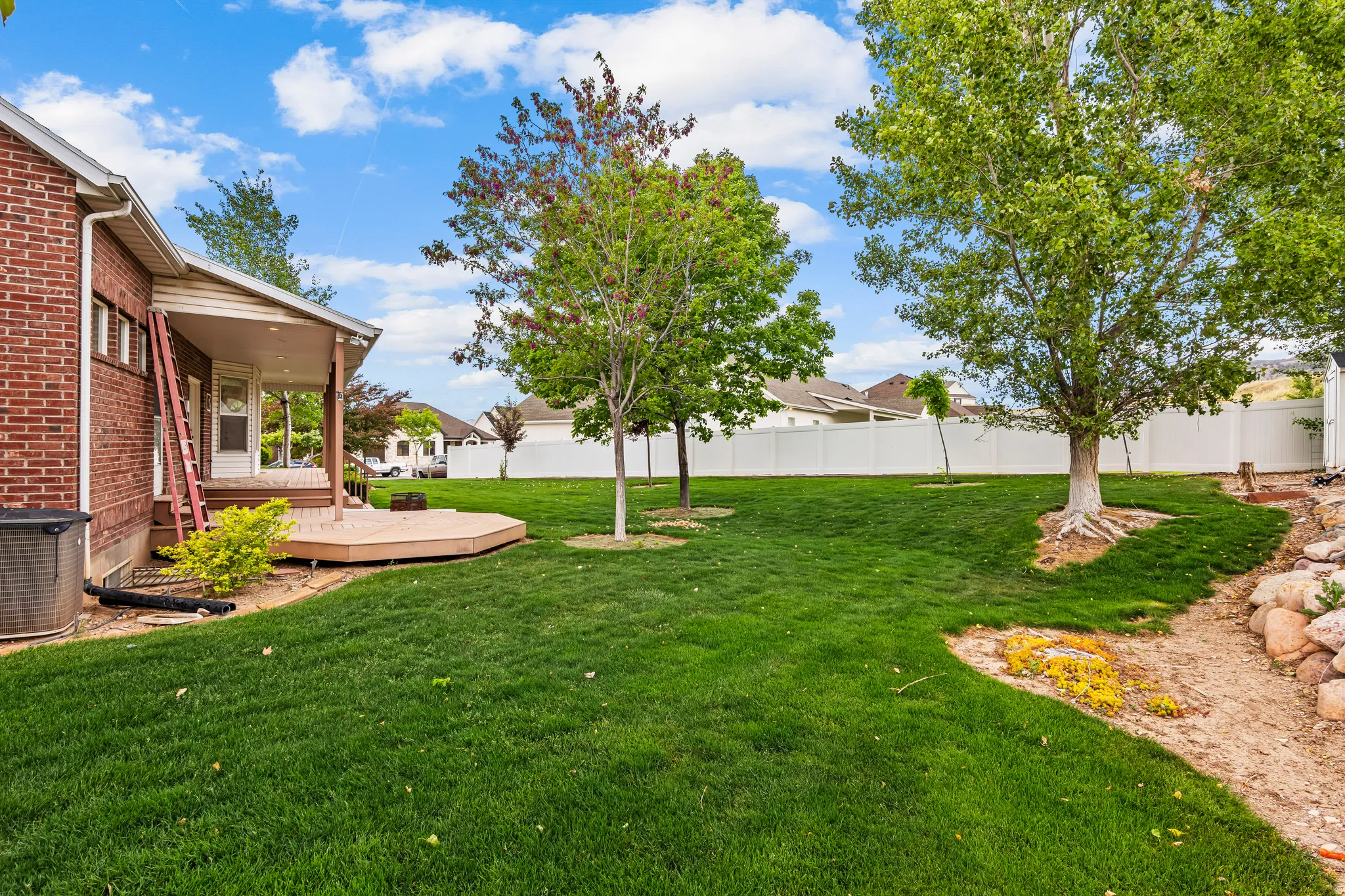 Spacious backyard featuring a covered patio, a multi-level composite deck, mature trees, and a white vinyl privacy fence