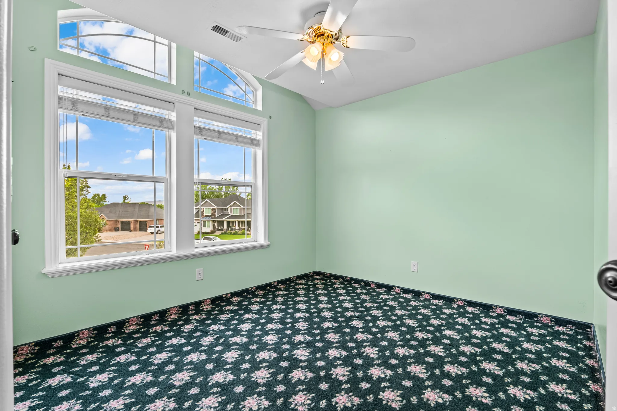 Room with a vaulted ceiling, patterned carpet flooring, and a ceiling fan with integrated lighting
