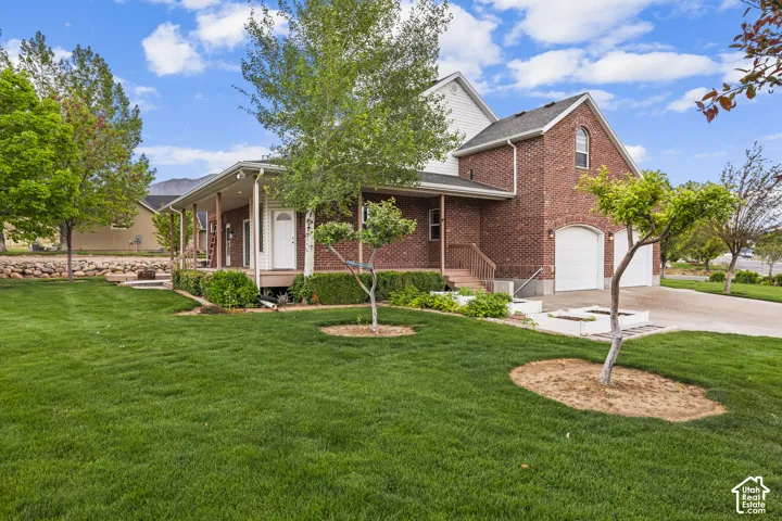 Brick and siding exterior featuring a covered porch with white columns, a two-car garage with arched entrances, mature trees, and a manicured lawn