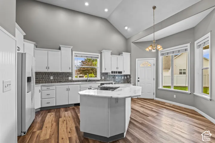 Modern kitchen featuring vaulted ceilings, recessed lighting, wood-finish flooring, a central island with a light-toned countertop, and white cabinetry with dark hardware