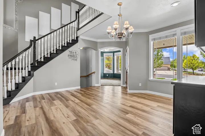 Expansive entry area featuring wood-finish flooring, a grand staircase with dark treads and white balusters, and a chandelier with glass shades