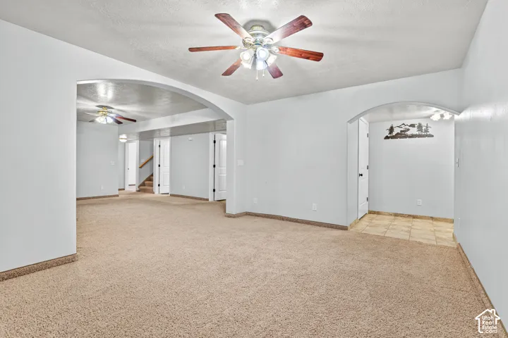 Spacious living area featuring neutral carpeting, light-toned walls, and a ceiling fan with wood-finish blades