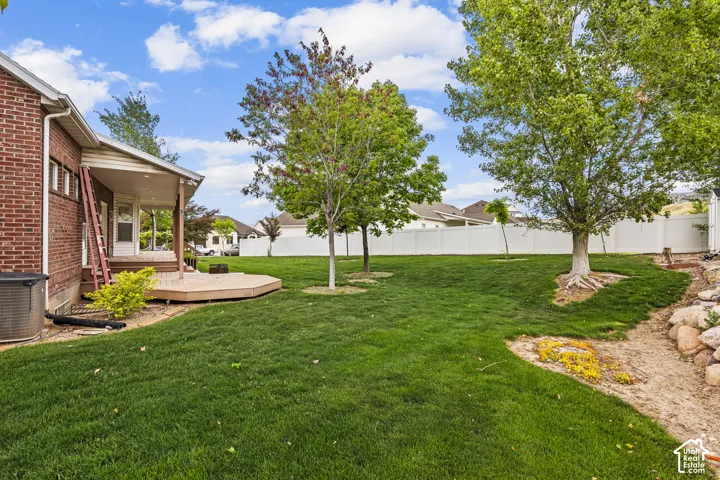 Spacious backyard featuring a covered patio, a multi-level composite deck, mature trees, and a white vinyl privacy fence