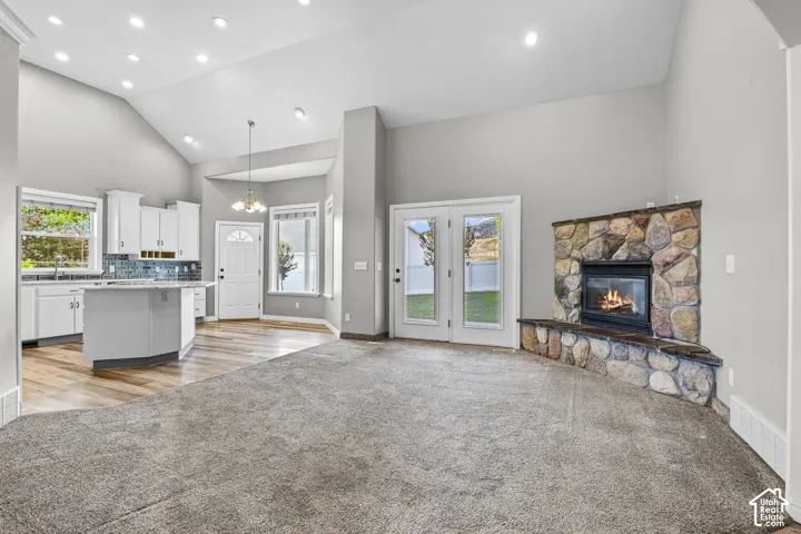 Spacious living area featuring a stone-clad fireplace and hearth, French doors, vaulted ceilings with recessed lighting, a kitchen island with seating, and wood-finish flooring