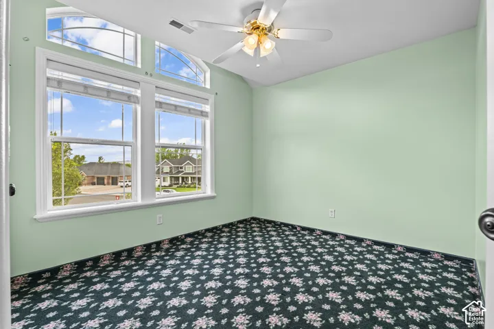 Room with a vaulted ceiling, patterned carpet flooring, and a ceiling fan with integrated lighting