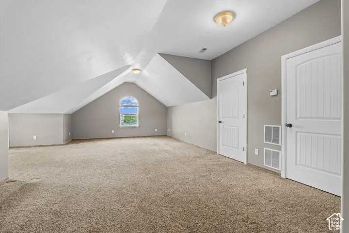 Spacious carpeted room featuring a vaulted ceiling with an arched window, two paneled doors, and ceiling-mounted lighting fixtures